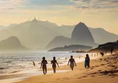 Niteroi, Brazil - February 10, 2016: Four girls taking a walk in Camboinhas beach. Sugar Loaf mountain and Christ the Redeemer statue on top of Corcovado mountain are present in the background.