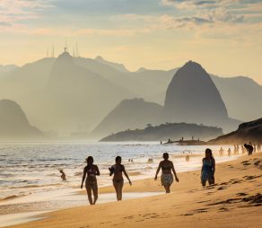 Niteroi, Brazil - February 10, 2016: Four girls taking a walk in Camboinhas beach. Sugar Loaf mountain and Christ the Redeemer statue on top of Corcovado mountain are present in the background.